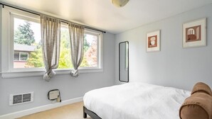 A bedroom with a bed, curtains, a window, a radiator, and framed pictures on the wall. - Delightful Urban Retreat (Seattle)