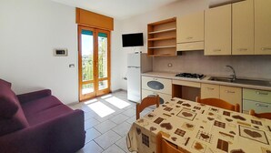 A compact kitchen with a dining area, a TV mounted above the stove, and a sliding glass door leading to a balcony. - Lovely apartment in Vieste with WiFi (Vieste)