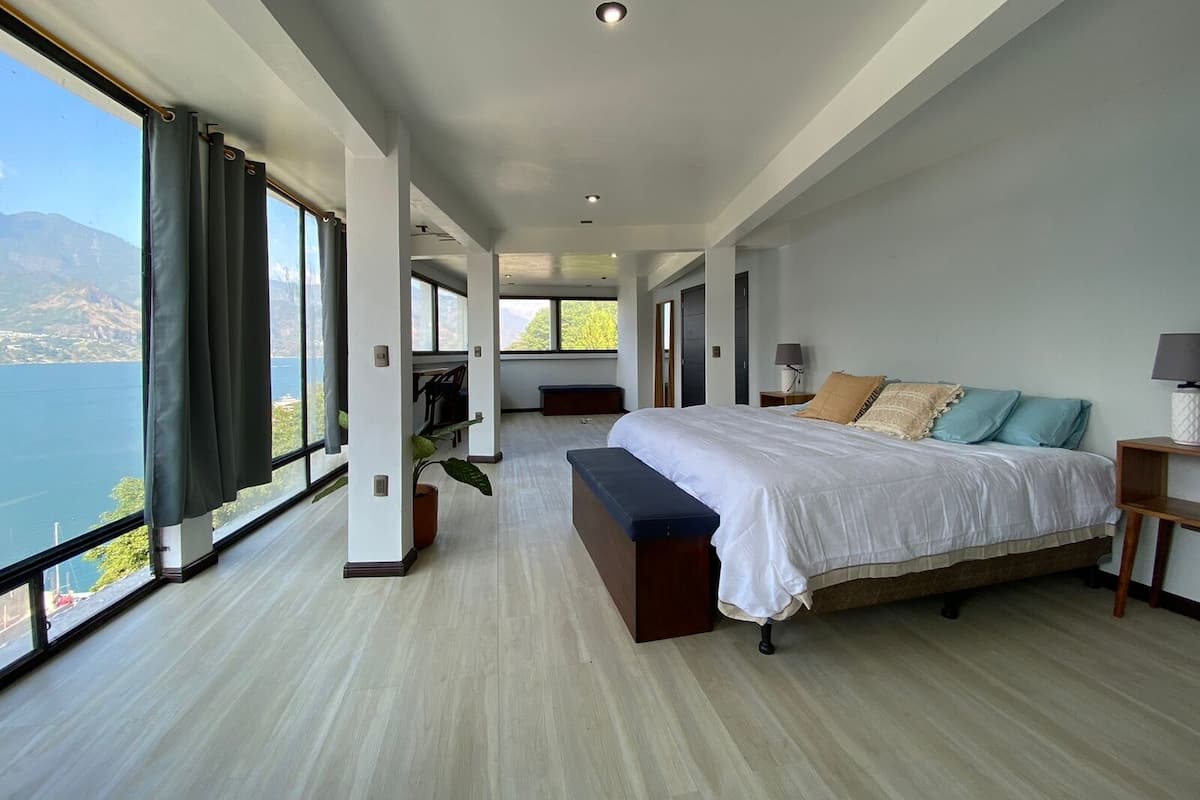 Un dormitorio amplio con una cama grande, un banco y vistas a un lago.