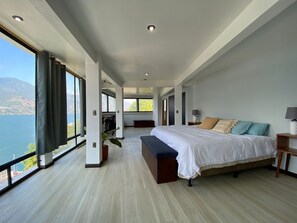 A spacious bedroom with a large bed, a bench, and a view of a lake. - Mónaco (San Pedro La Laguna)