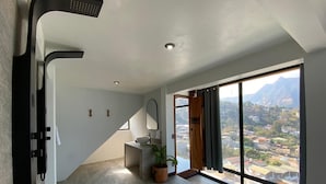 Un baño moderno con un ventanal grande, ducha, lavamanos y una planta en maceta.