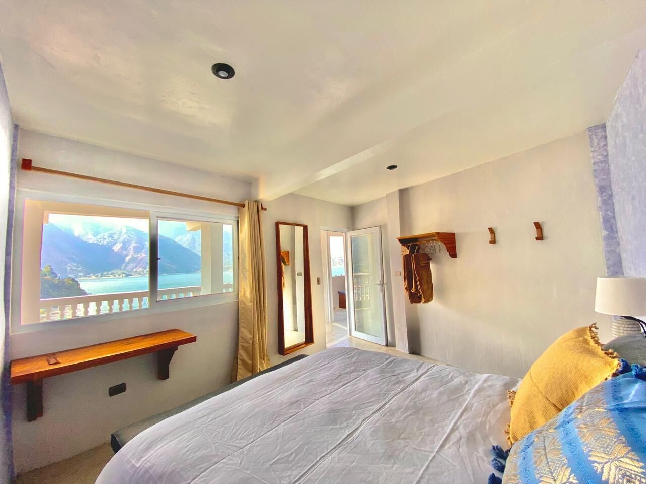 Quarto com cama, um banquinho, espelho e janela com vista para montanhas.