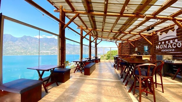 Un restaurante con vistas al mar y a las montañas, que cuenta con mesas y bancos de madera, y un letrero que dice "Monaco Penthouse".