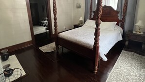 Una cama con dosel y tablero de madera, un candelabro y un espejo grande en la pared.