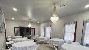 Un salón de conferencias con mesas redondas, sillas blancas y candelabros.