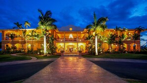 A two-story hotel with a central entrance, palm trees, and a well-lit driveway.