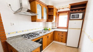 A compact kitchen with wooden cabinets, a gas stove, a microwave, and a built-in oven. - Apartment El Arco, in Conil. (Conil)