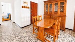A dining area with a wooden table and chairs, a wooden cabinet with glass doors, and a door with a coat rack. - Apartment El Arco, in Conil. (Conil)
