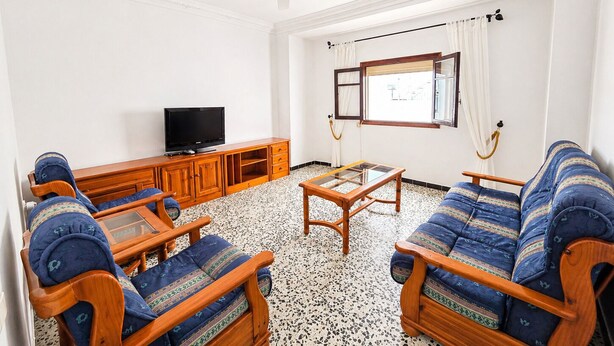 A living room with a television, wooden furniture, a ceiling fan, and a window with curtains. - Apartment El Arco, in Conil. (Conil)