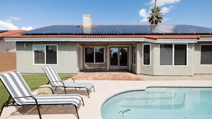 Uma casa com piscina, painéis solares e um pátio com espreguiçadeiras.