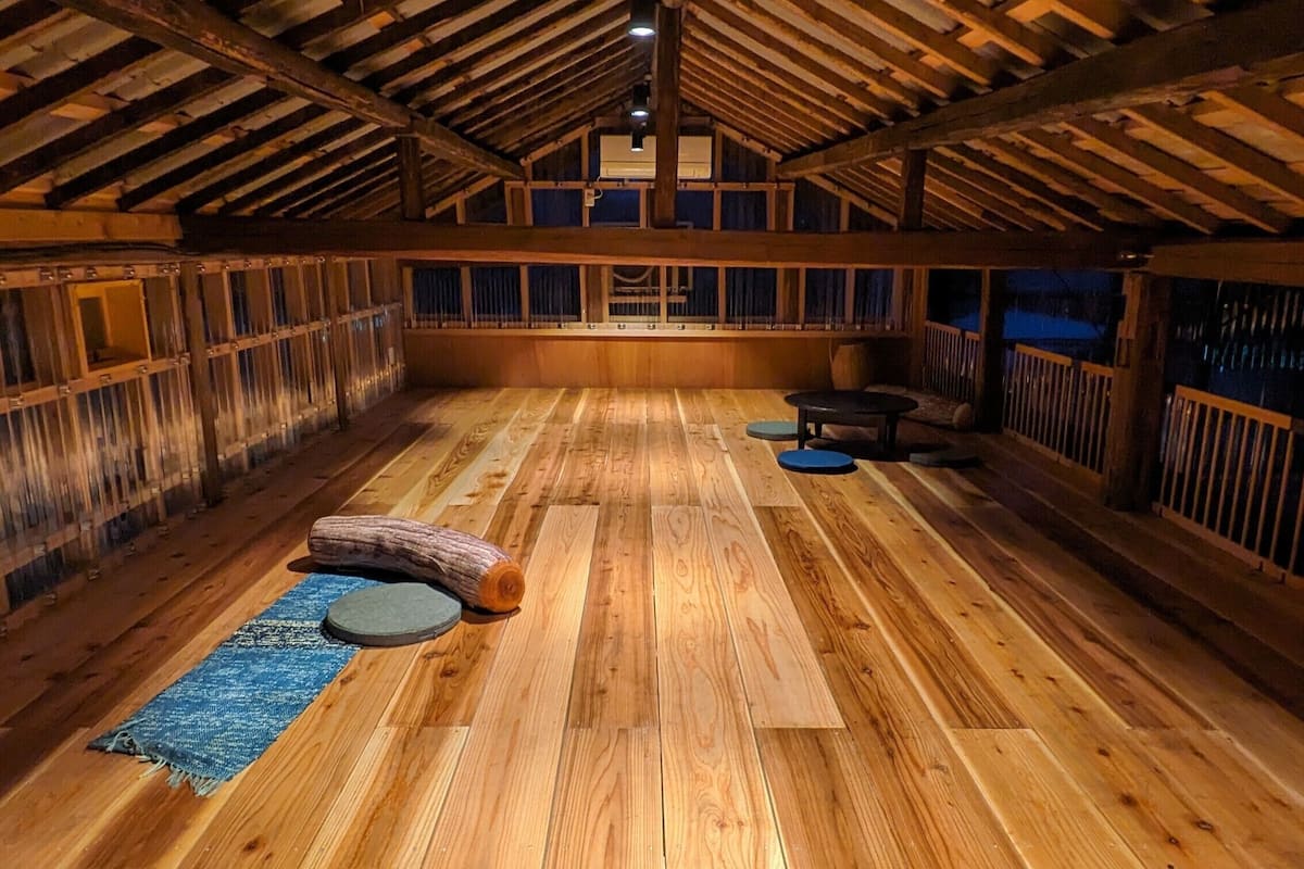 Ein geräumiges Dachzimmer mit Holzböden, einem großen Fenster und einer Holzbalkendecke.
