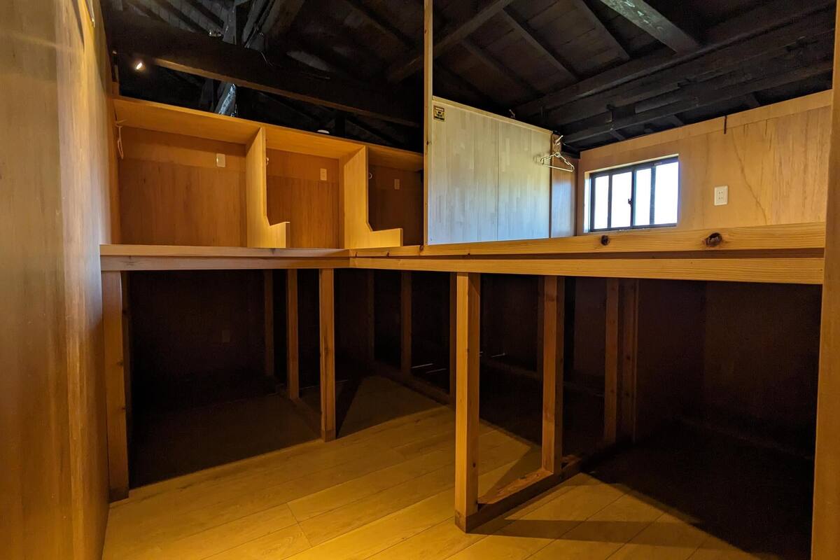 Ein Zimmer mit freiliegenden Holzbalken, einem vergitterten Fenster und einem Holzboden.