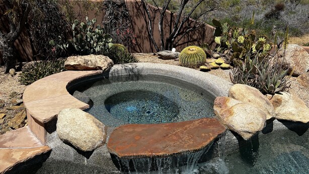 Banyera d'hidromassatge envoltada de roques i cactus en un jardí desert.