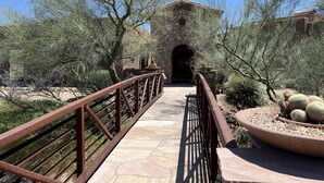 Un camí de pedra que condueix a un edifici de pedra amb una entrada apuntada, envoltat de cactus i arbres.