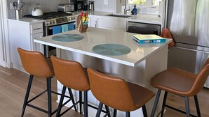 Eine moderne Küche mit weißen Schränken, Edelstahlgeräten und einer zentralen Kochinsel mit Barhocker.