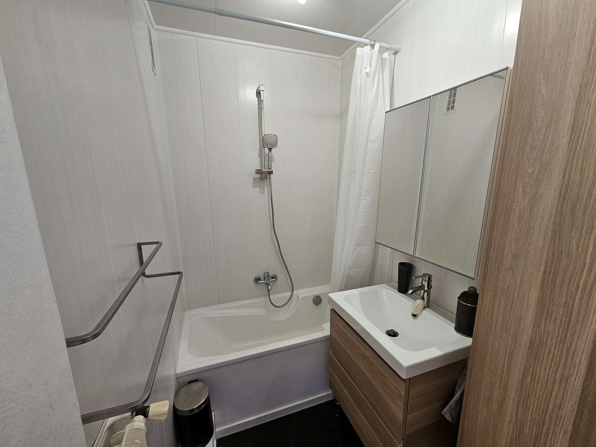 Een moderne badkamer met een bad, een douche en een wastafel met spiegel.