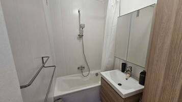 Een moderne badkamer met een bad, een douche en een wastafel met spiegel.