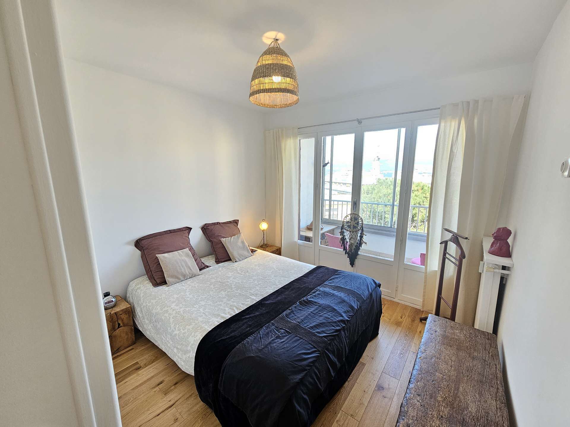 Une chambre à coucher avec un lit, un luminaire suspendu, une fenêtre avec des rideaux et un balcon avec une chaise.