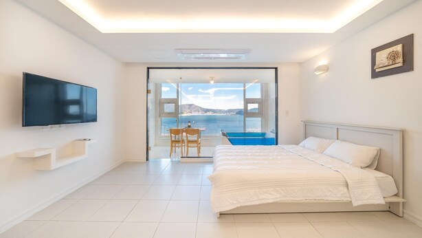 Een moderne slaapkamer met een bed, een televisie, uitzicht op zee en een balkon met een tafel en stoelen.