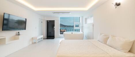 Ein modernes Schlafzimmer mit einem großen Bett, einem Flachbildfernseher, einer Badewanne und Meerblick.