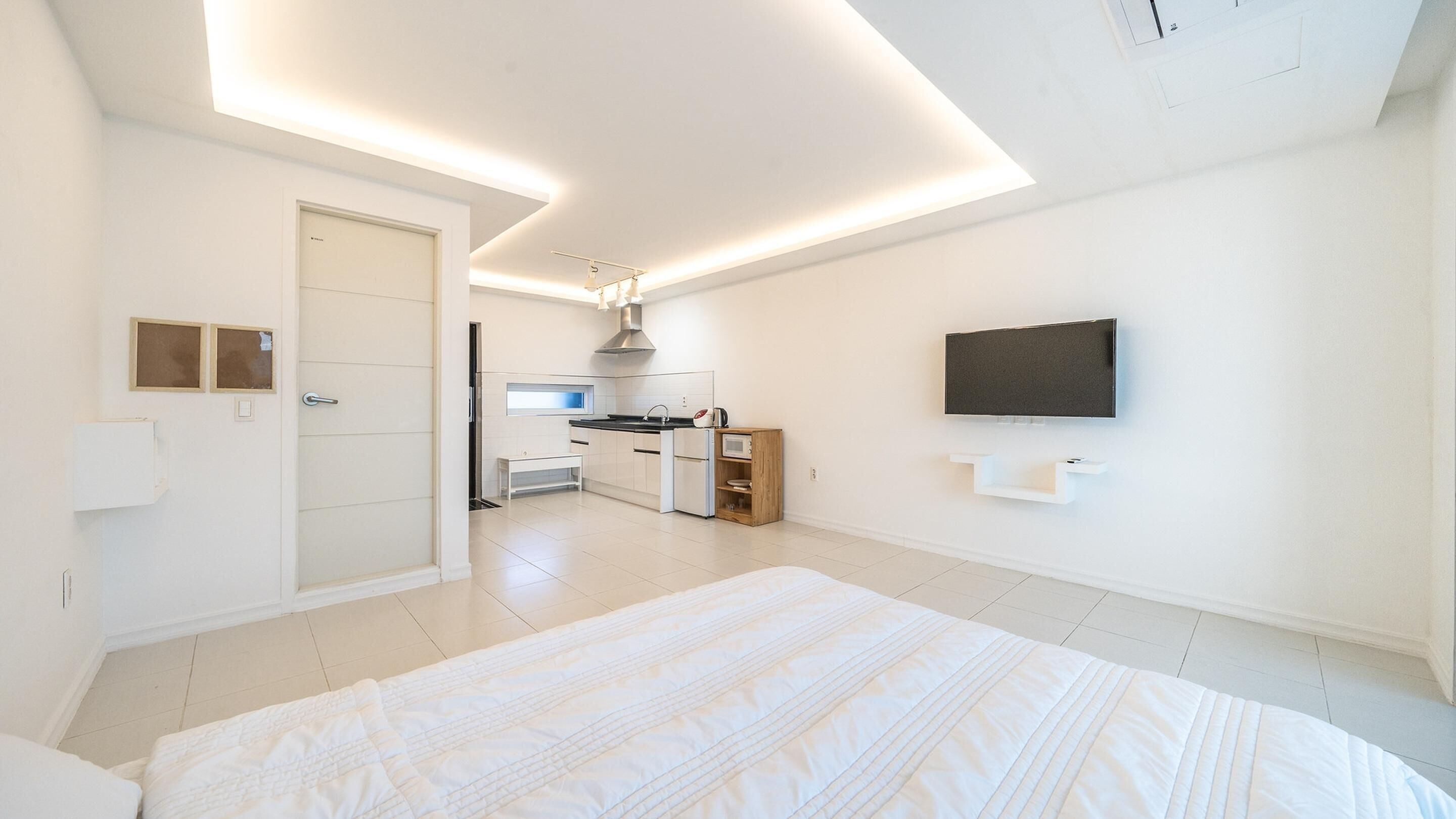 Habitación de hotel moderna con una cama grande, una kitchenette, un televisor montado en la pared y una puerta que da a otra habitación.