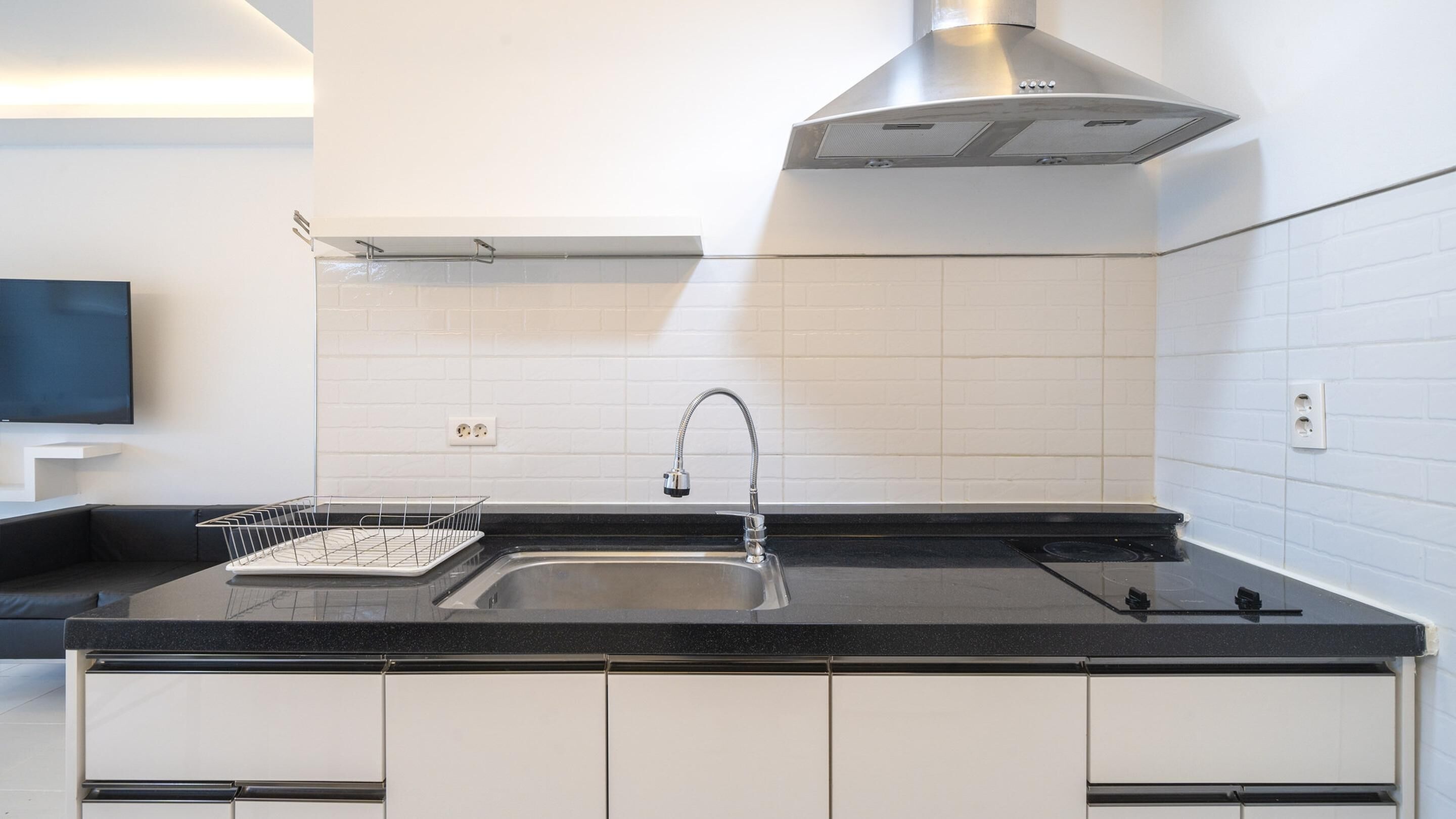 A modern kitchen with a stainless steel sink, black countertop, white cabinets, and a stainless steel range hood.