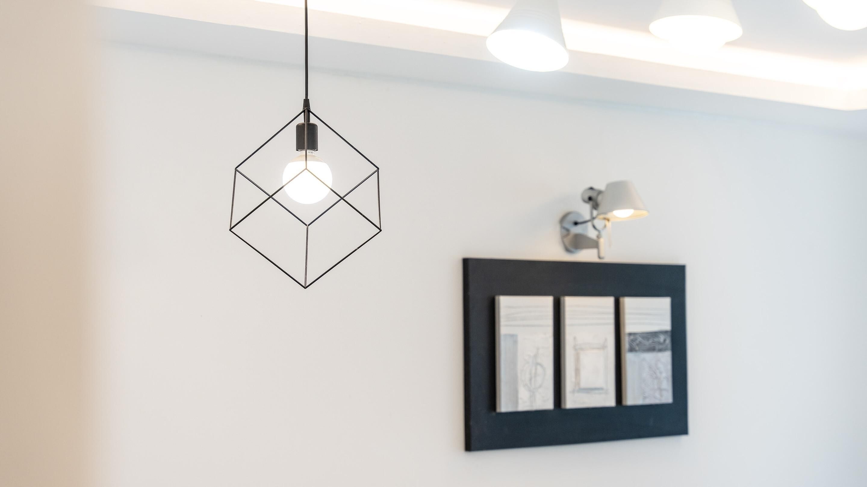Un intérieur moderne agrémenté d’un luminaire suspendu aux formes géométriques, d’une œuvre d’art encadrée et d’une lampe fixée au mur.
