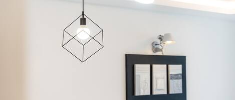 Un intérieur moderne agrémenté d’un luminaire suspendu aux formes géométriques, d’une œuvre d’art encadrée et d’une lampe fixée au mur.