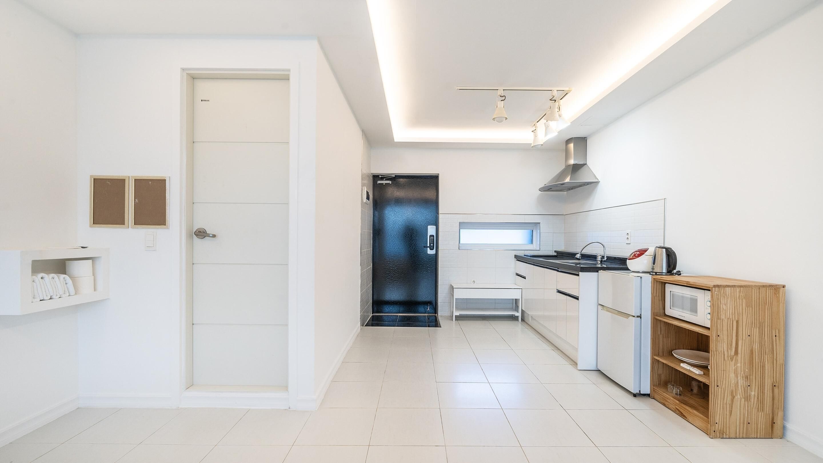 A modern kitchen with white cabinetry, a black door, and a wooden shelf unit.