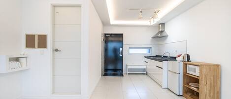 A modern kitchen with white cabinetry, a black door, and a wooden shelf unit.