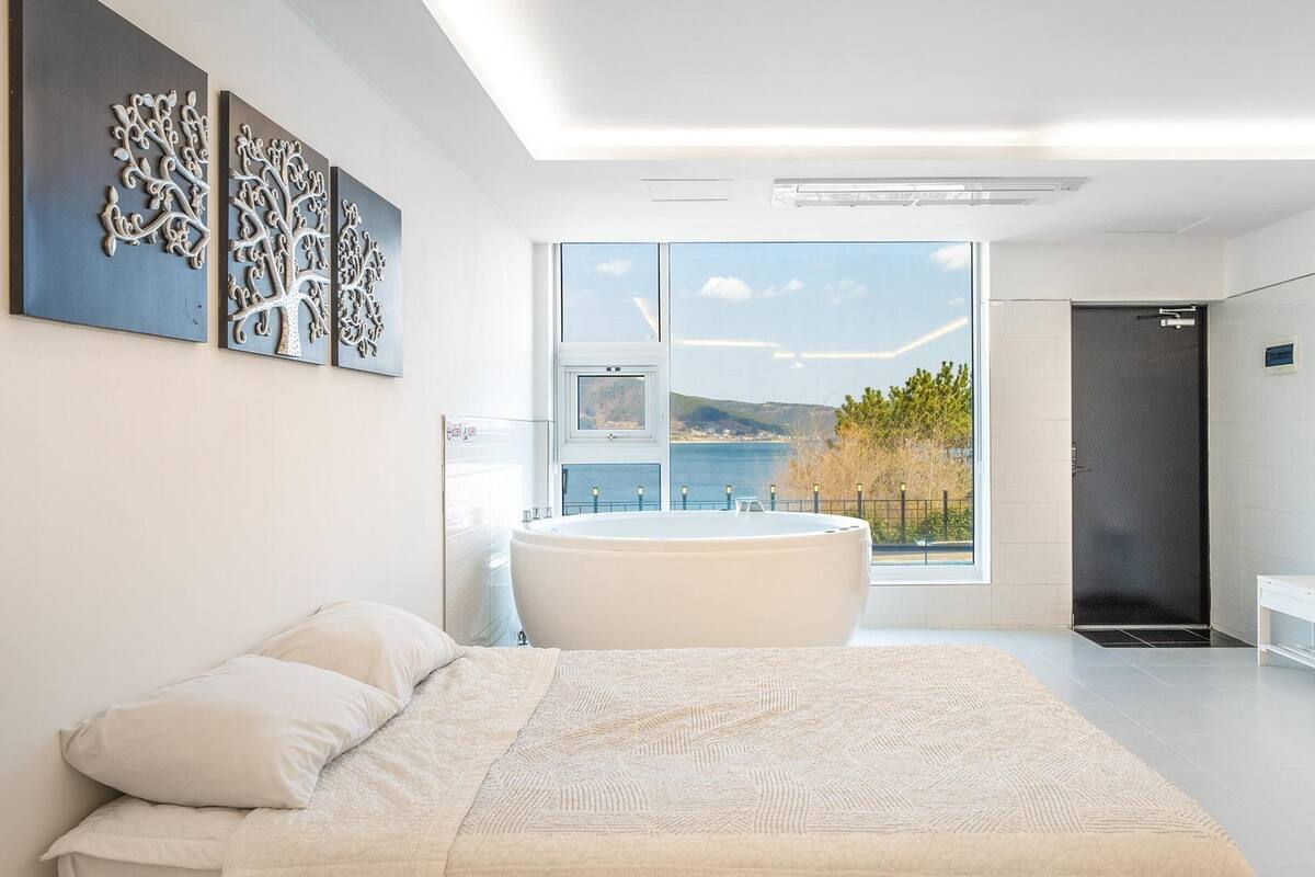 A modern bedroom with a large bed, a bathtub, and a view of a body of water.