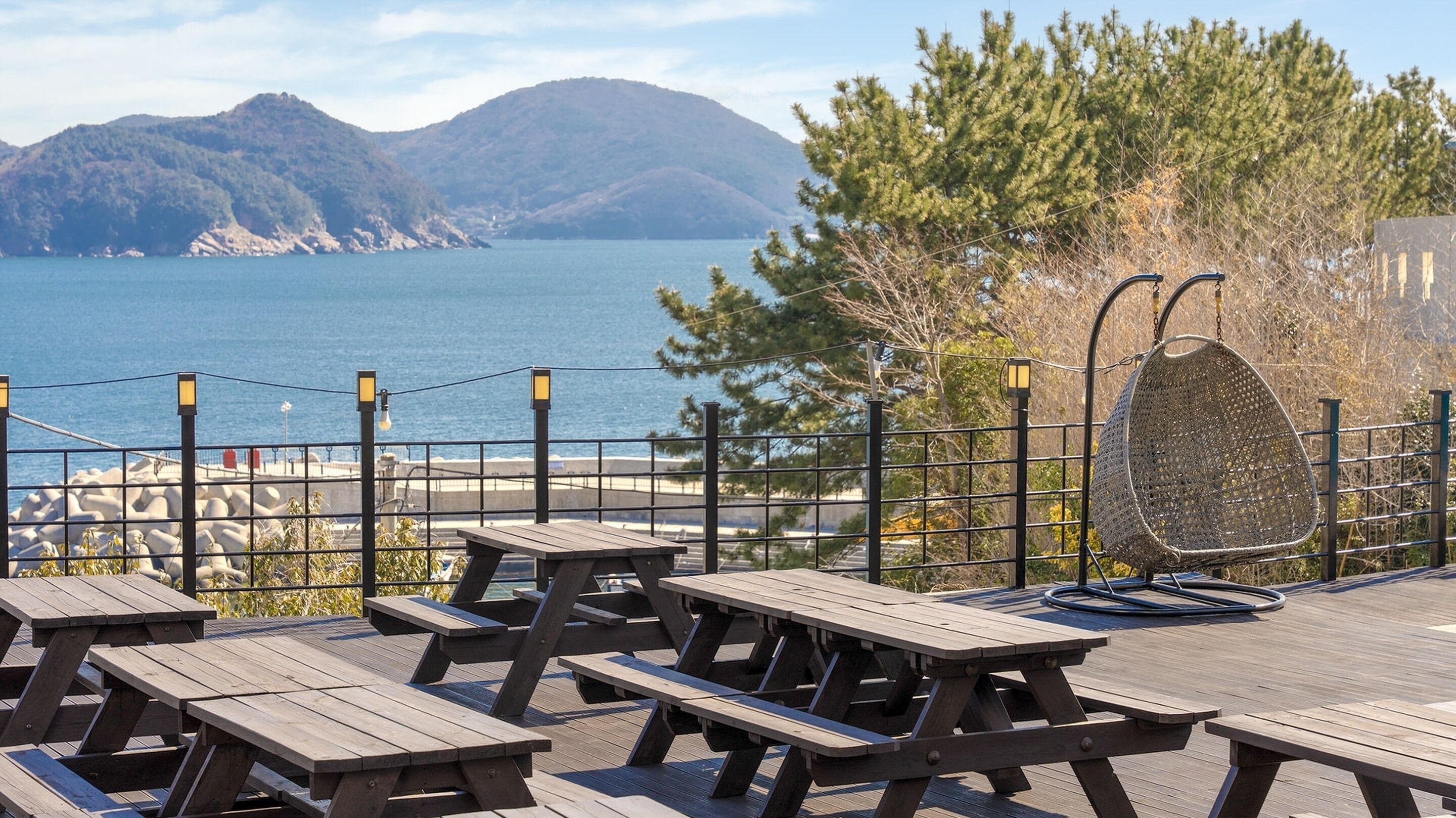 A wooden deck with picnic tables overlooking a body of water and mountains.