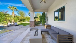 An outdoor patio with a fire pit, seating, and a view of a pool and garden.
