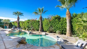 A pool area with two pools, lounge chairs, palm trees, and a well-maintained garden.