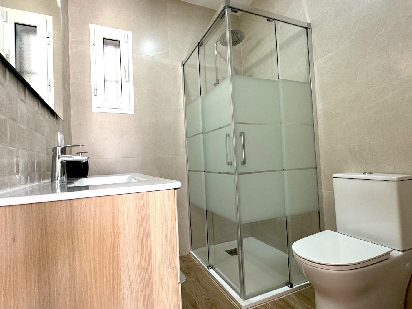Un baño moderno con ducha de vidrio, inodoro y lavamanos con encimera.