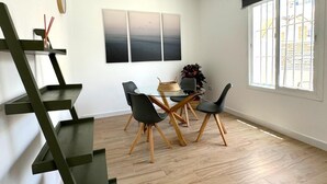 A dining area with a table and chairs, a painting on the wall, and a window with bars. - SibsSanlucar Guadalquivir (Sanlúcar de Barrameda)