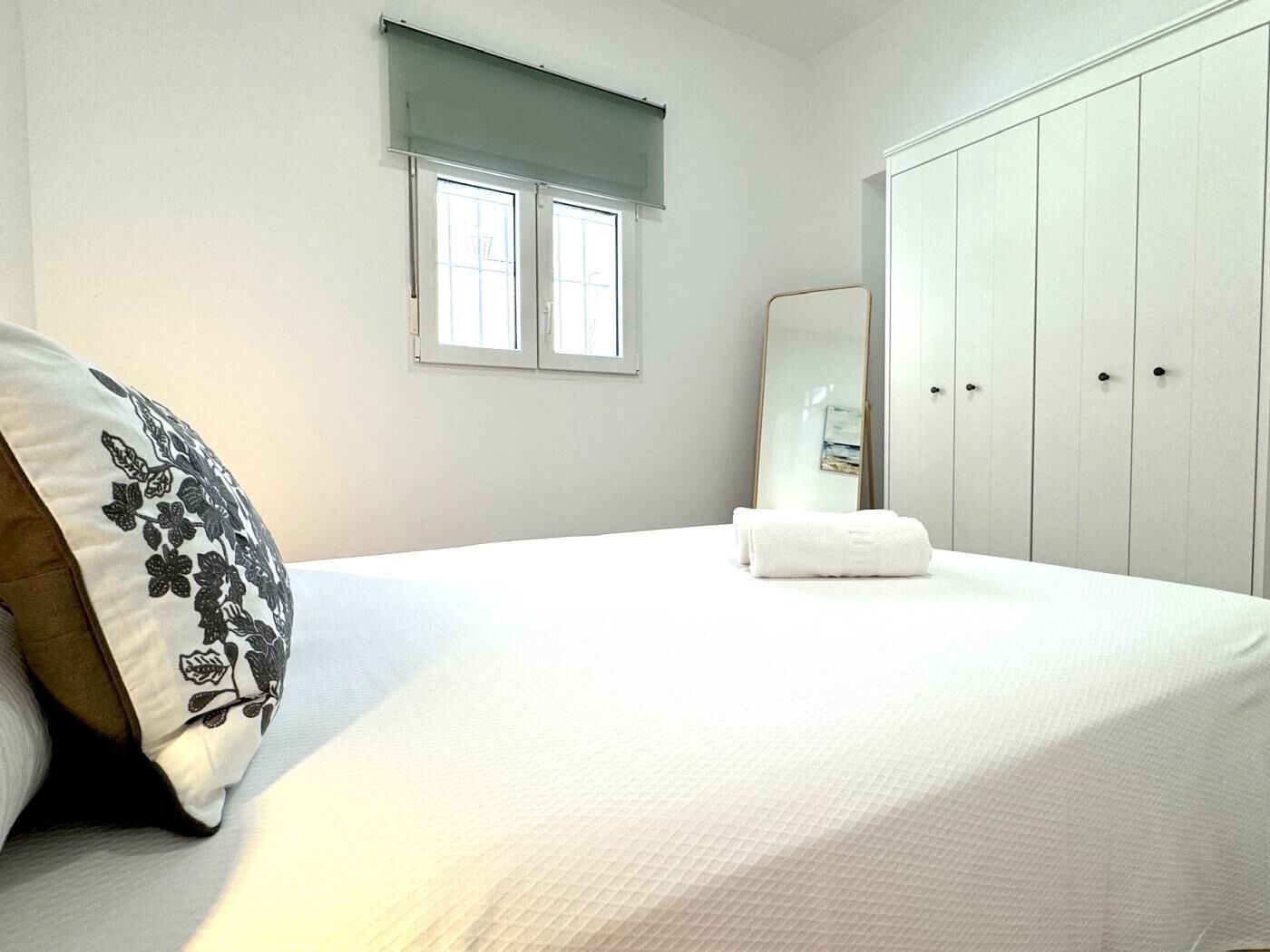 A bedroom with a bed, a bedside table, a mirror, and a wardrobe.