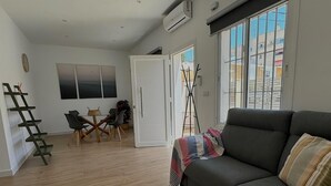 A modern living room with a sofa, a dining table with chairs, and a large window with a view of buildings. - SibsSanlucar Guadalquivir (Sanlúcar de Barrameda)