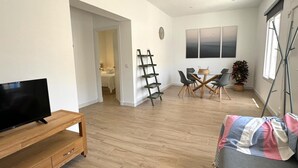 A modern living room with a TV on a wooden stand, a dining area with a table and chairs, a ladder against the wall, and a plant in the corner. - SibsSanlucar Guadalquivir (Sanlúcar de Barrameda)