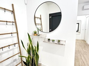 Ein modernes Interieur mit einer Holzleiter, einem runden Spiegel und kleinen Topfpflanzen an einer weißen Wand.