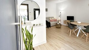 Ett modernt vardagsrum med en rund spegel, en soffa, ett matbord med stolar och en tv.