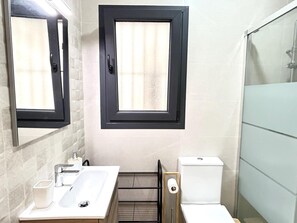 Une salle de bain avec un grand miroir, une fenêtre, un lavabo, des toilettes et une douche.