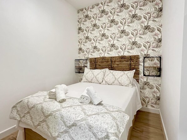 Un lit bien fait, avec une couvre-lit à motifs et des oreillers, une tête de lit en bois et deux appliques murales.