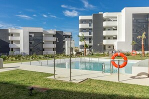 A modern building with a swimming pool, surrounded by a well-maintained lawn and palm trees.