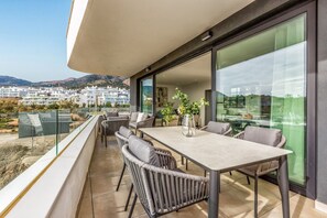 A balcony with a dining table and chairs, overlooking a residential area with buildings and hills.