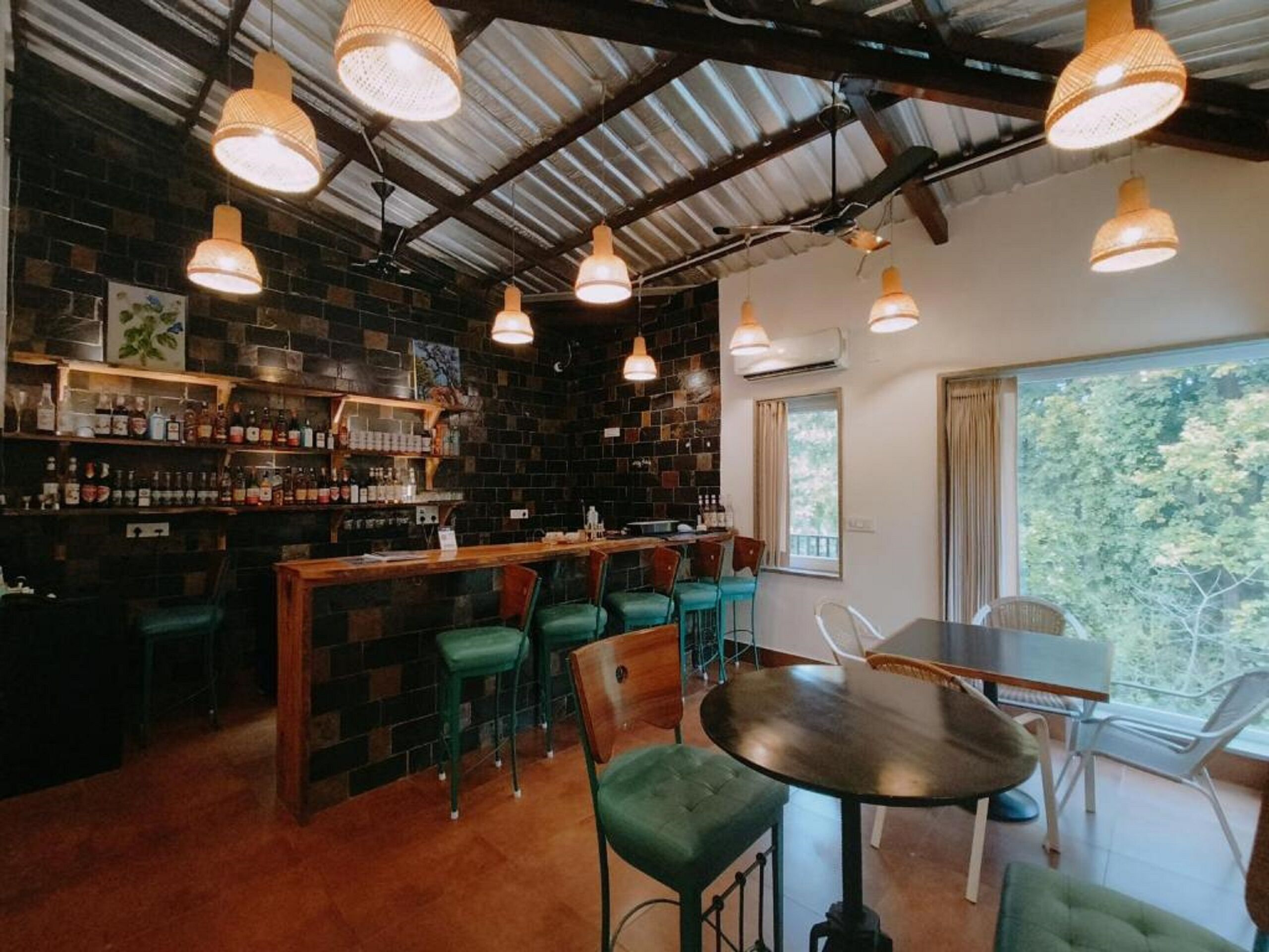 A bar area with a brick wall, green chairs, and hanging lights.