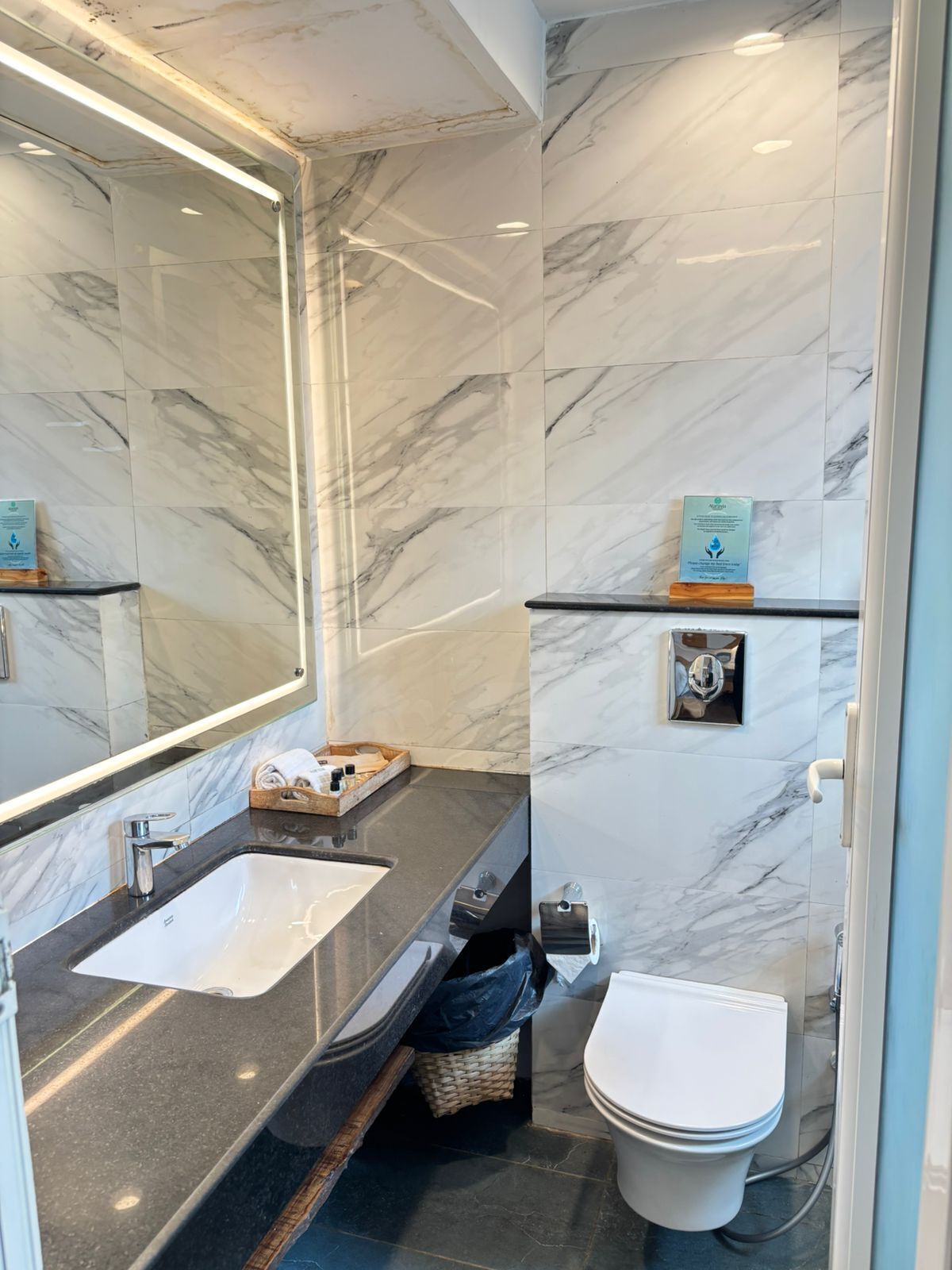 Et moderne badeværelse med marmor bagvæg, et stort spejl, en håndvask og et toilet.