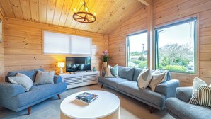 A cozy living room with wooden walls, two sofas, a coffee table, and a TV. -  located in the heart of Oneroa, landscaped garden and 5 minute's walk to beach (Waiheke Island)