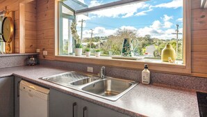 A kitchen with a double stainless steel sink, wooden cabinets, and a window with a view of the outdoors. -  located in the heart of Oneroa, landscaped garden and 5 minute's walk to beach (Waiheke Island)