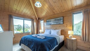 A wooden-paneled bedroom with a bed, bedside lamps, and a painting. -  located in the heart of Oneroa, landscaped garden and 5 minute's walk to beach (Waiheke Island)